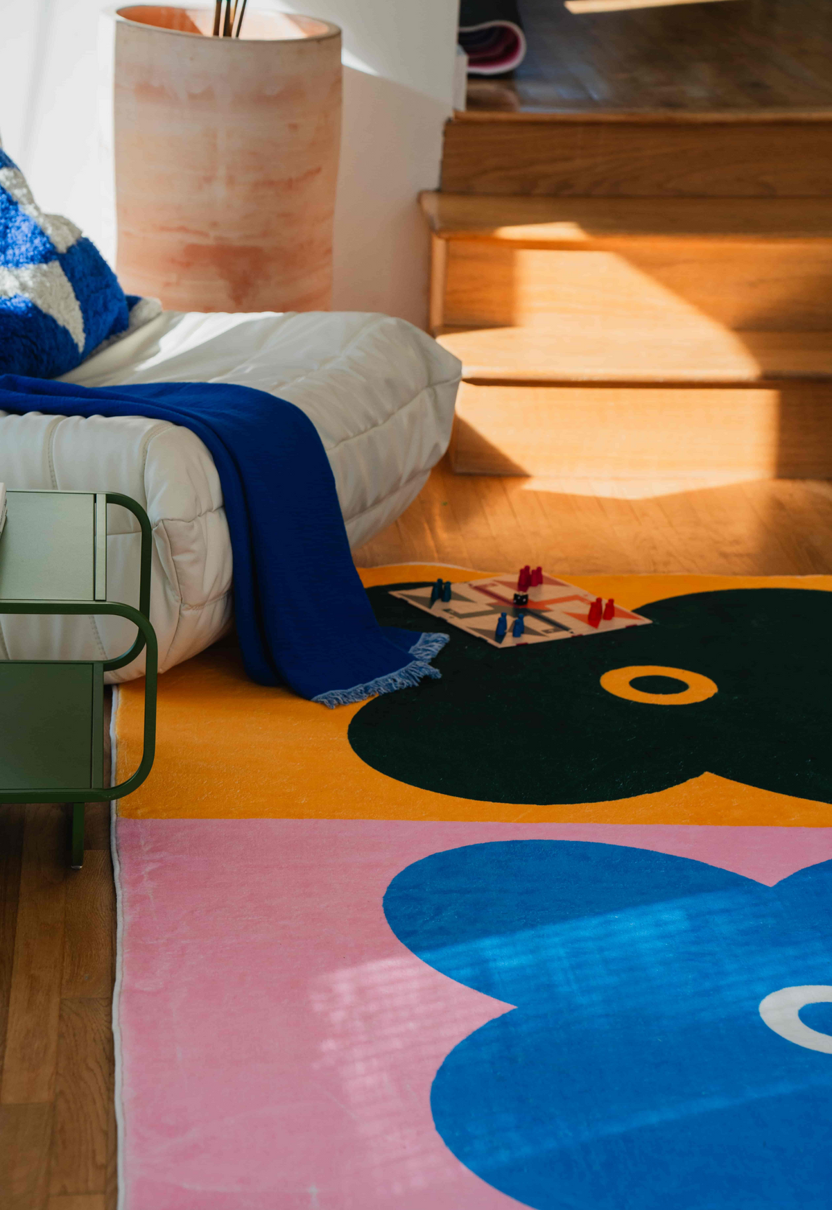 Pink and blue clover rug corner view with wood flooring, showing part of green clover and cozy seating area.