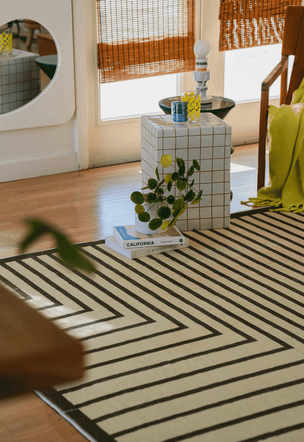 Close-up of rug's striped corner pattern beside a white grid stool, green chair, and yellow throw.