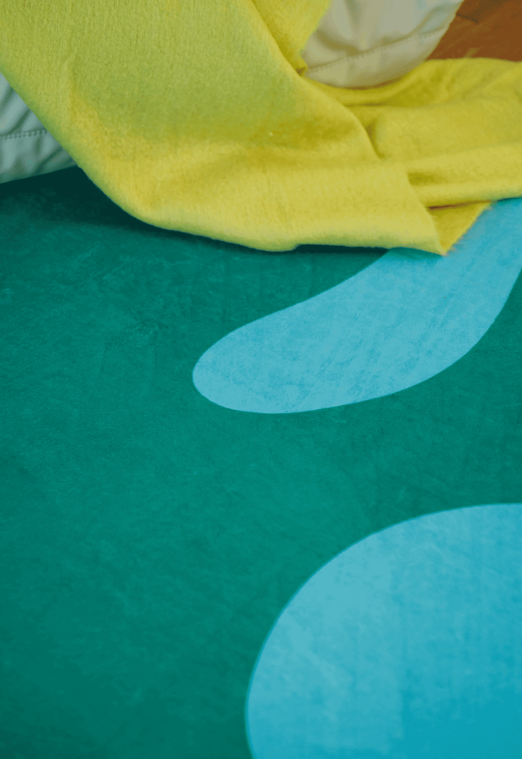 Detail of rug texture and organic shape, partially covered by yellow throw and cushions on wooden floor.