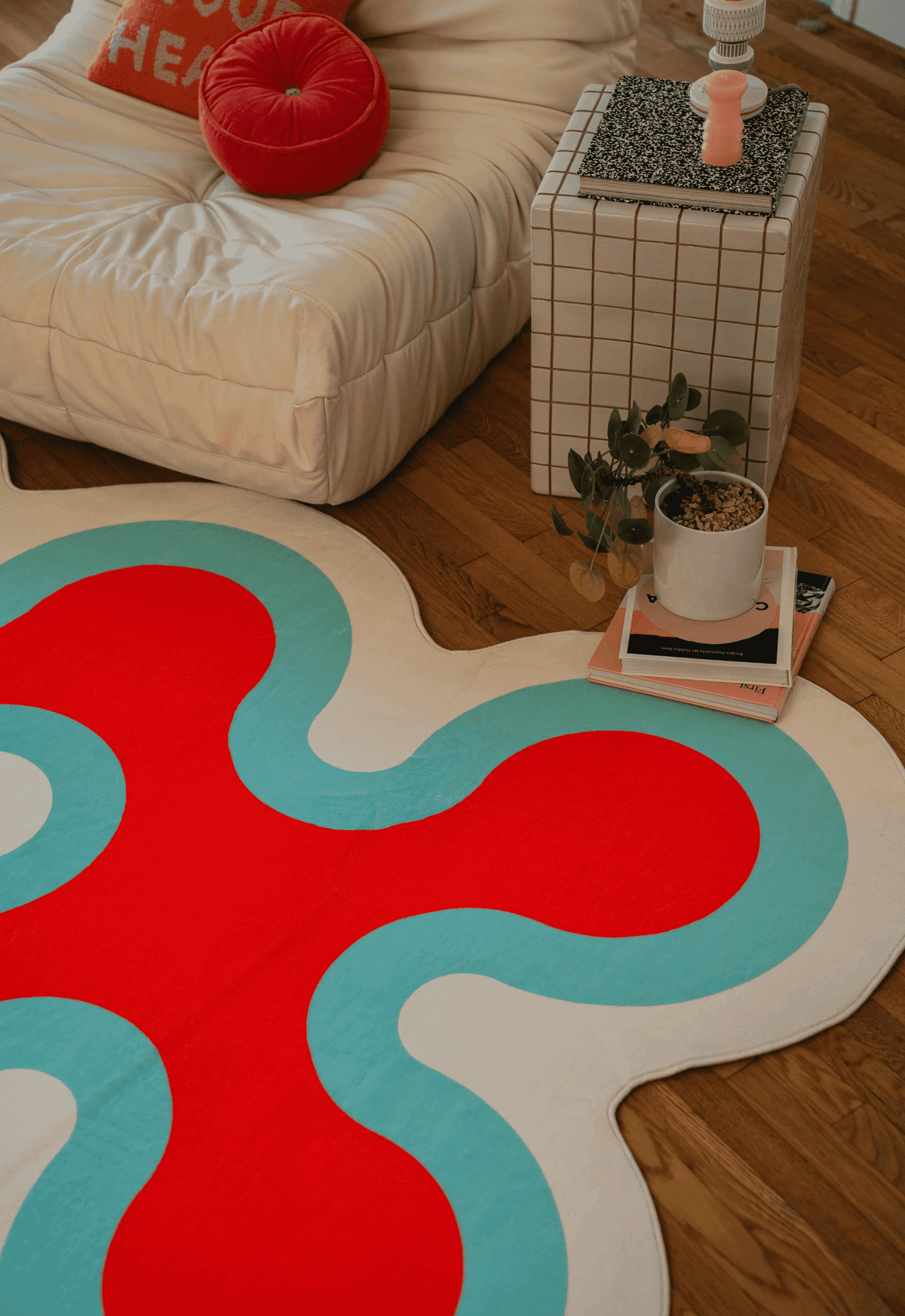 Corner detail of coral-patterned rug in pink with cream and aqua edges beneath side table.