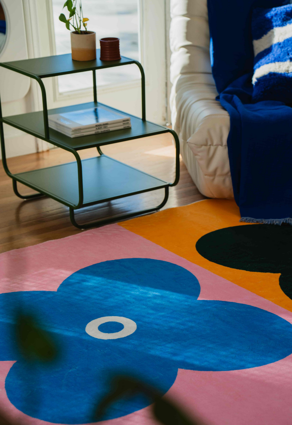 Close-up of a blue clover motif on a pink background from the multicolor four leaf clover rug next to a green side table.