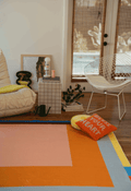 Living room scene with a white armchair, grid side table, and Modern Geometric Print Rug in orange, pink, blue, and yellow.