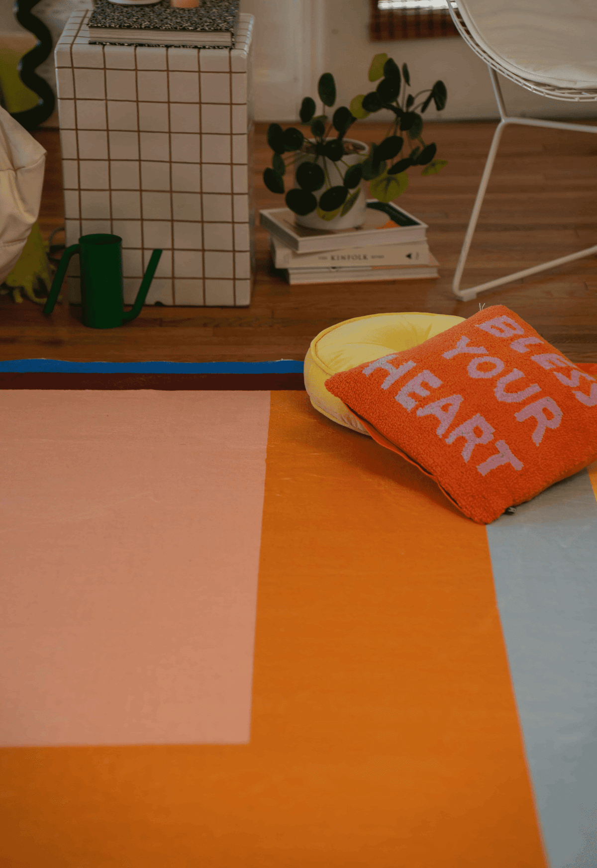 Close-up of colorful rug corner with “Bless Your Heart” pillow and lemon-shaped cushion on geometric orange and pink background.