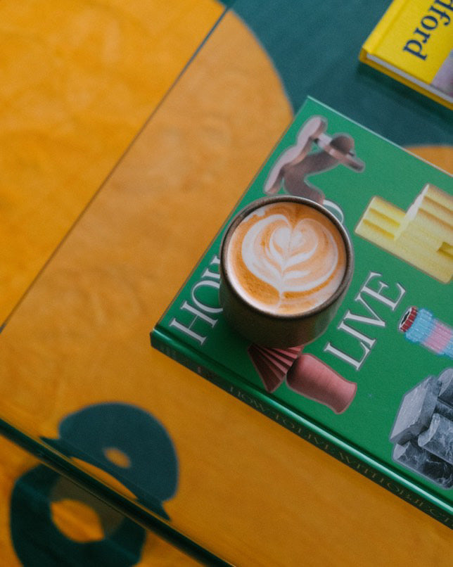 Yellow clover petal detail under coffee table with design books and latte, showcasing rug's plush surface and color play.