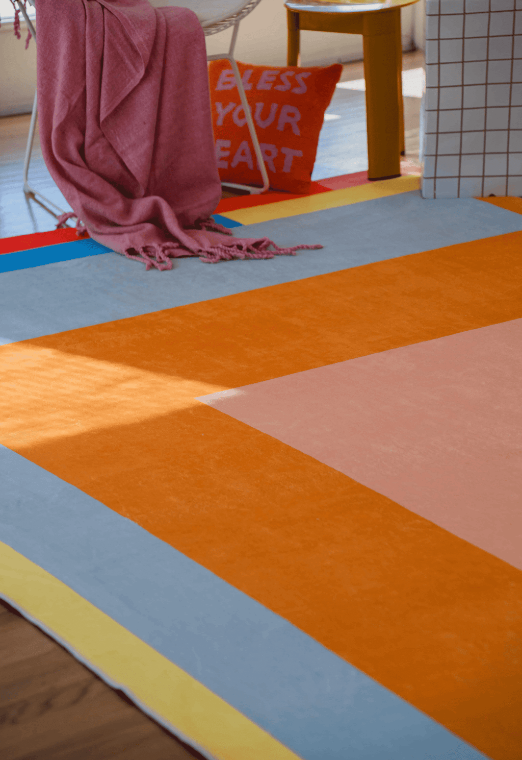 Close-up of the colorful rug’s orange and pink central panels framed by blue, yellow, and gray blocks under a pink blanket.