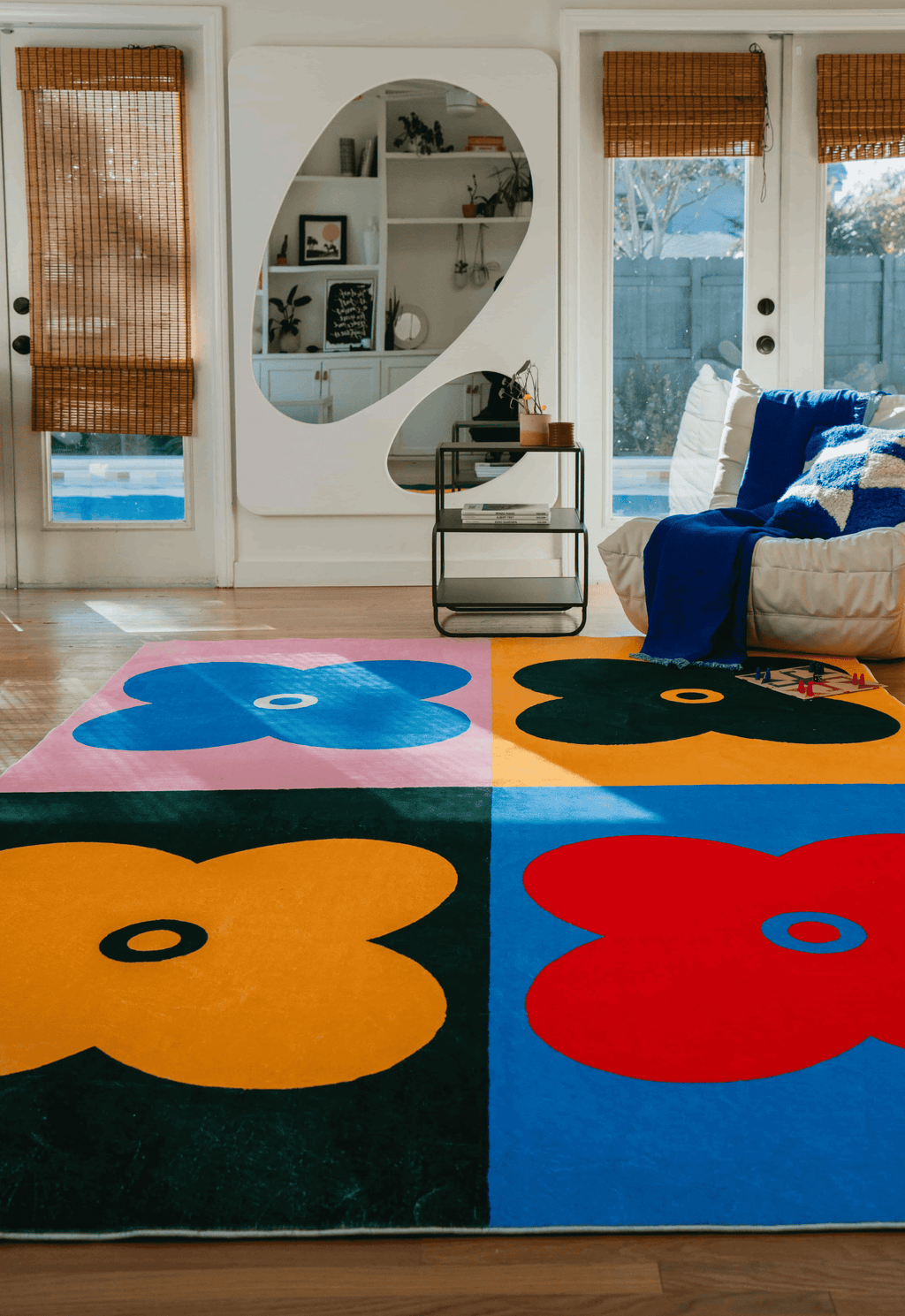 Full view of the multicolor four leaf clover rug laid in a sunlit living room with a white sofa and large mirror cabinet.