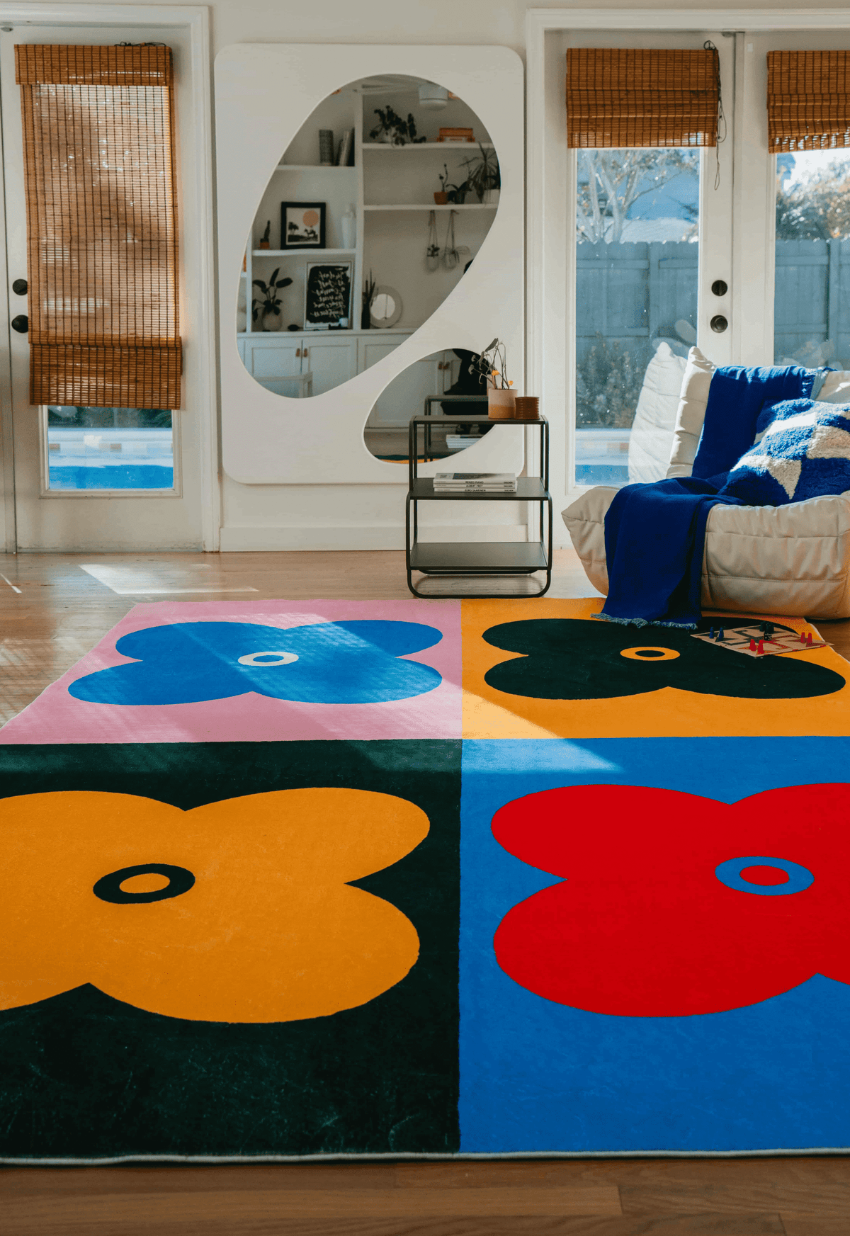 Full view of the multicolor four leaf clover rug laid in a sunlit living room with a white sofa and large mirror cabinet.
