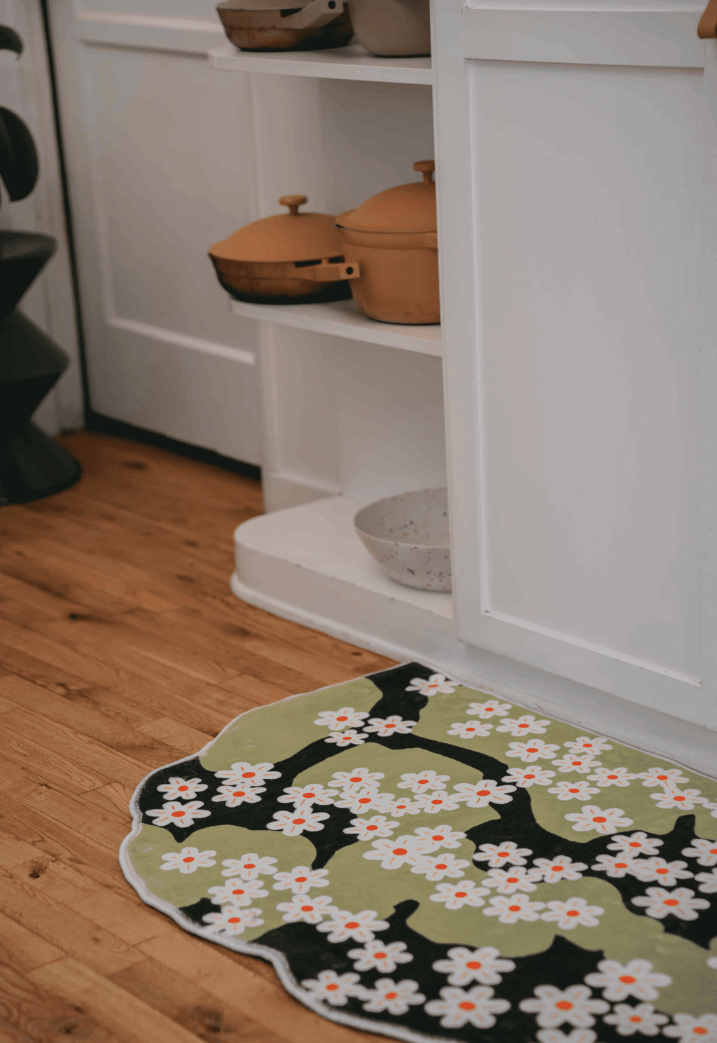 Irregular Daisy in Summer Rug placed along the base of a white cabinet, on warm wood floor near built-in shelving.