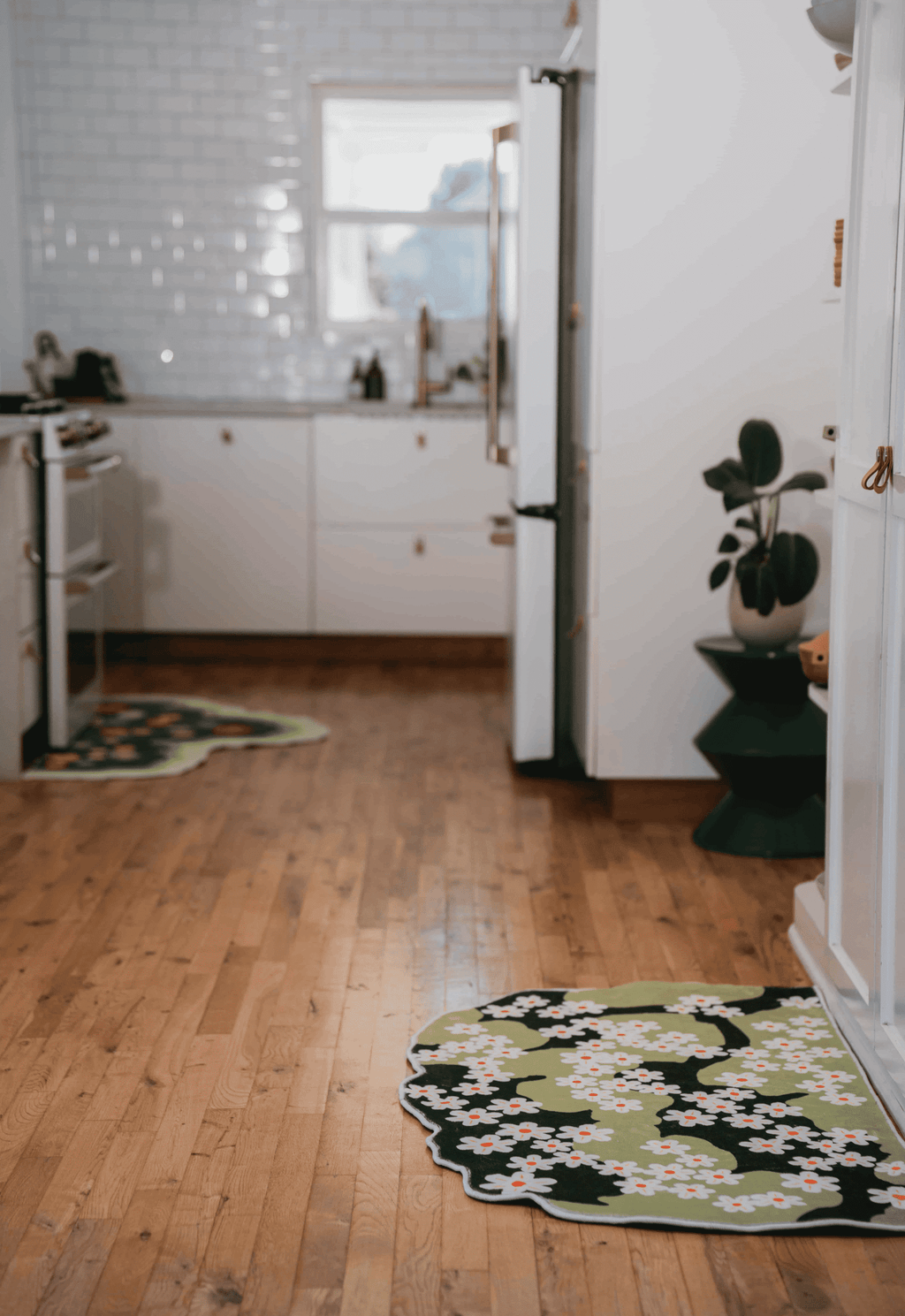 Two daisy rugs spread across wood floor in a long kitchen aisle, placed beside counters and cabinet edges.