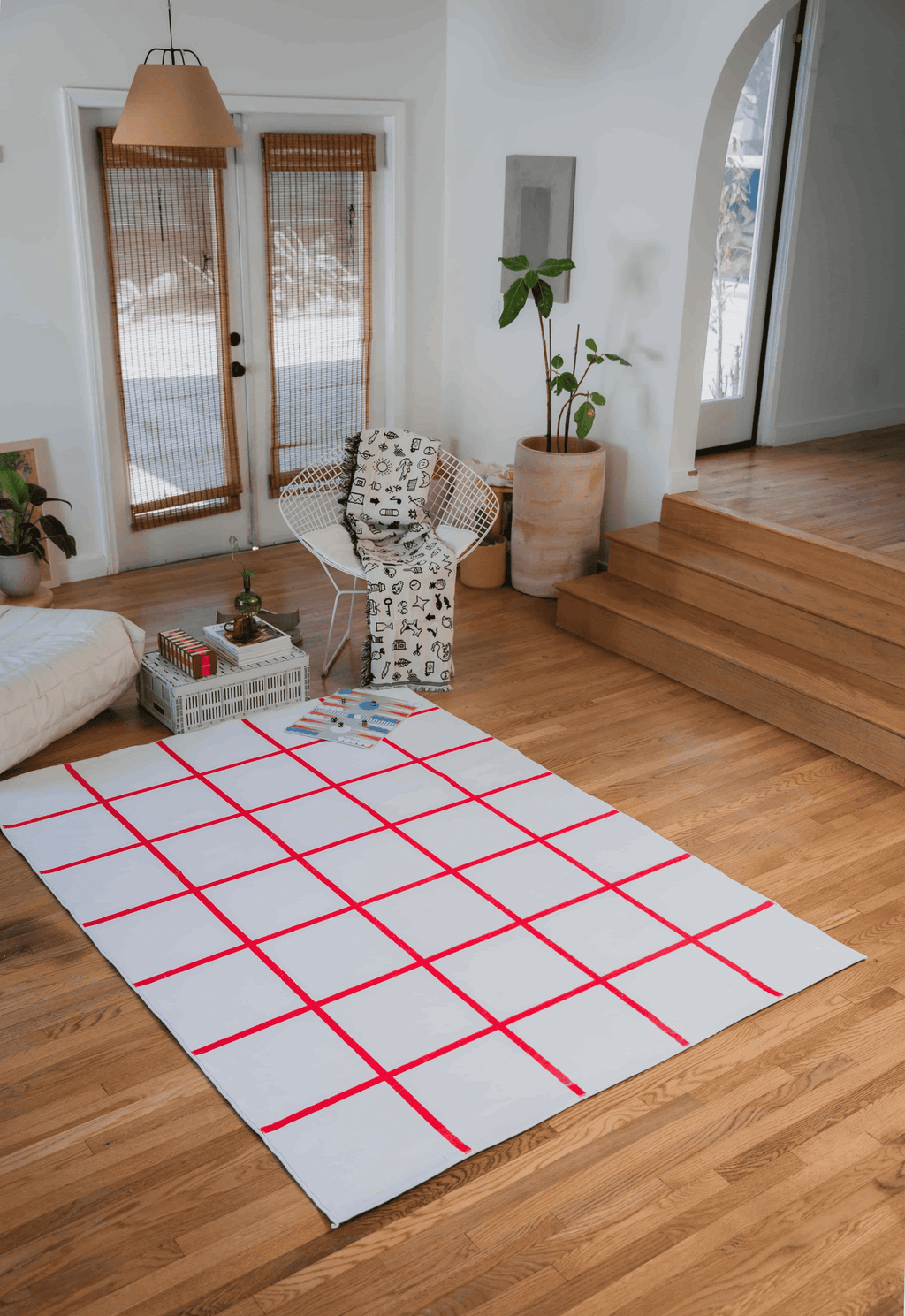 Red and White Grid Modern Design Rug by Johann Banta placed in sunlit living room with white chair and potted plants by the archway.