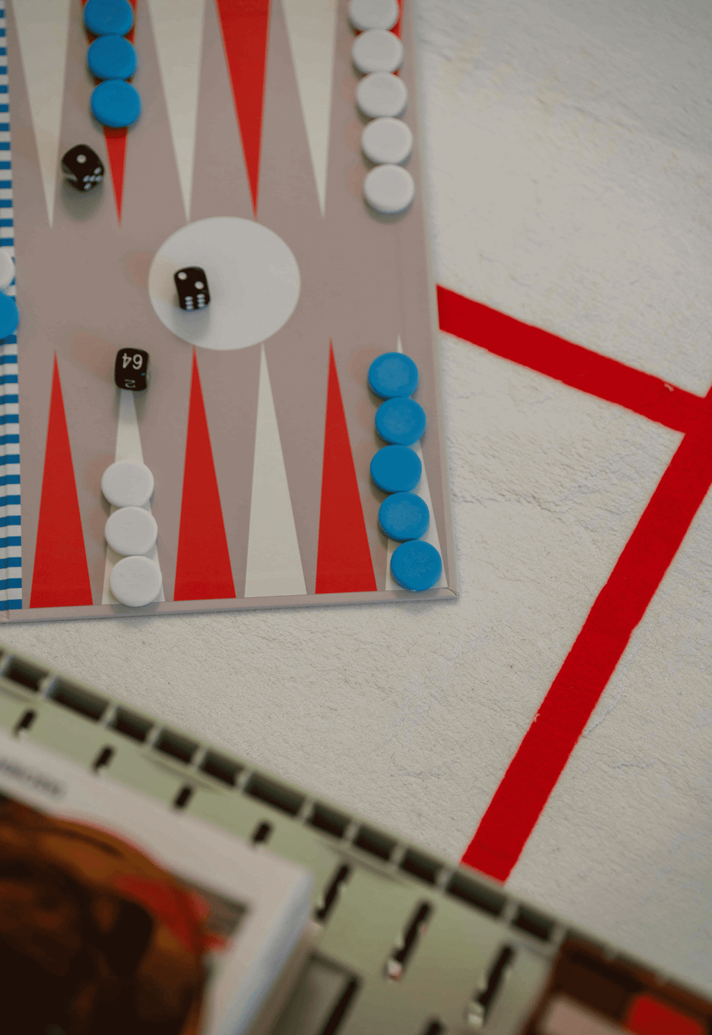 Close-up of backgammon set placed on red grid rug near crate side table and art books.