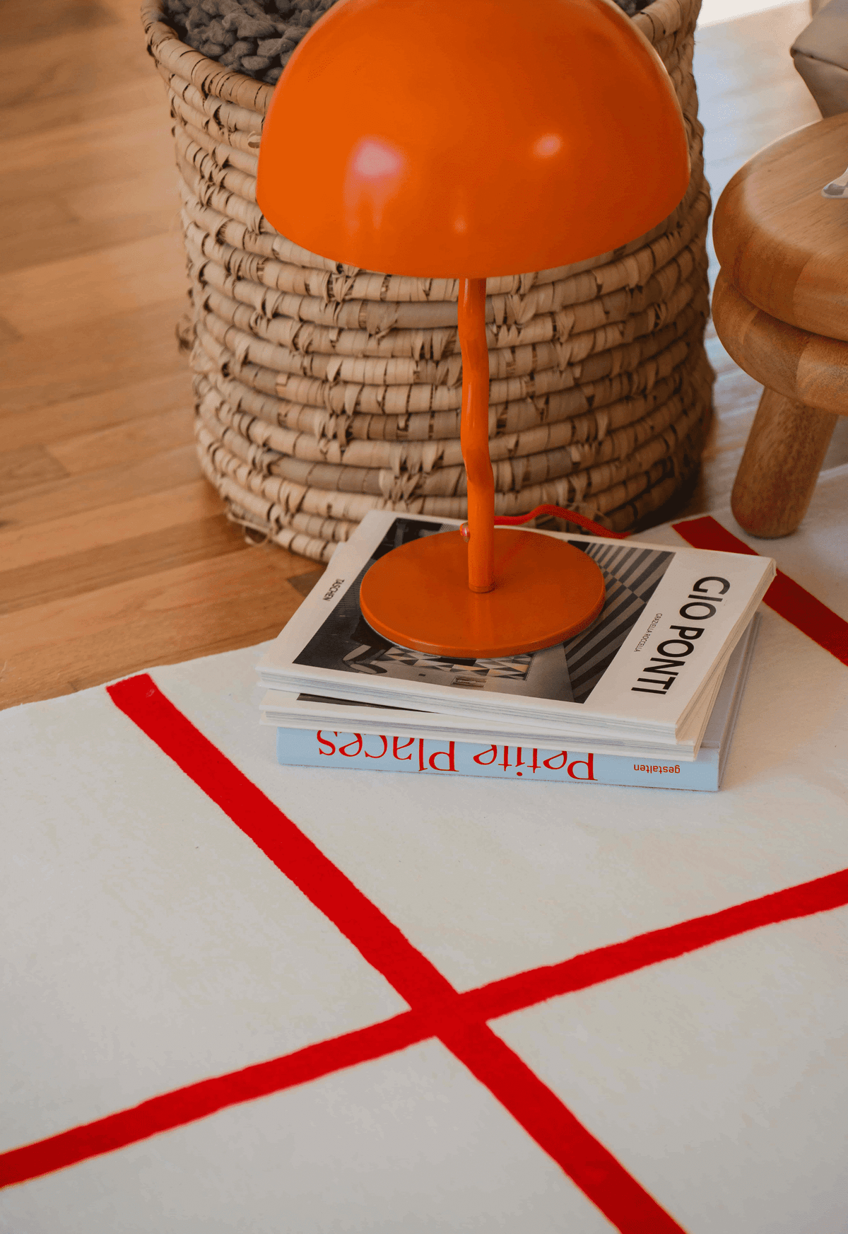 Close-up of red grid lines under orange table lamp and stacked books, showcasing rug texture and contrast in cozy corner.