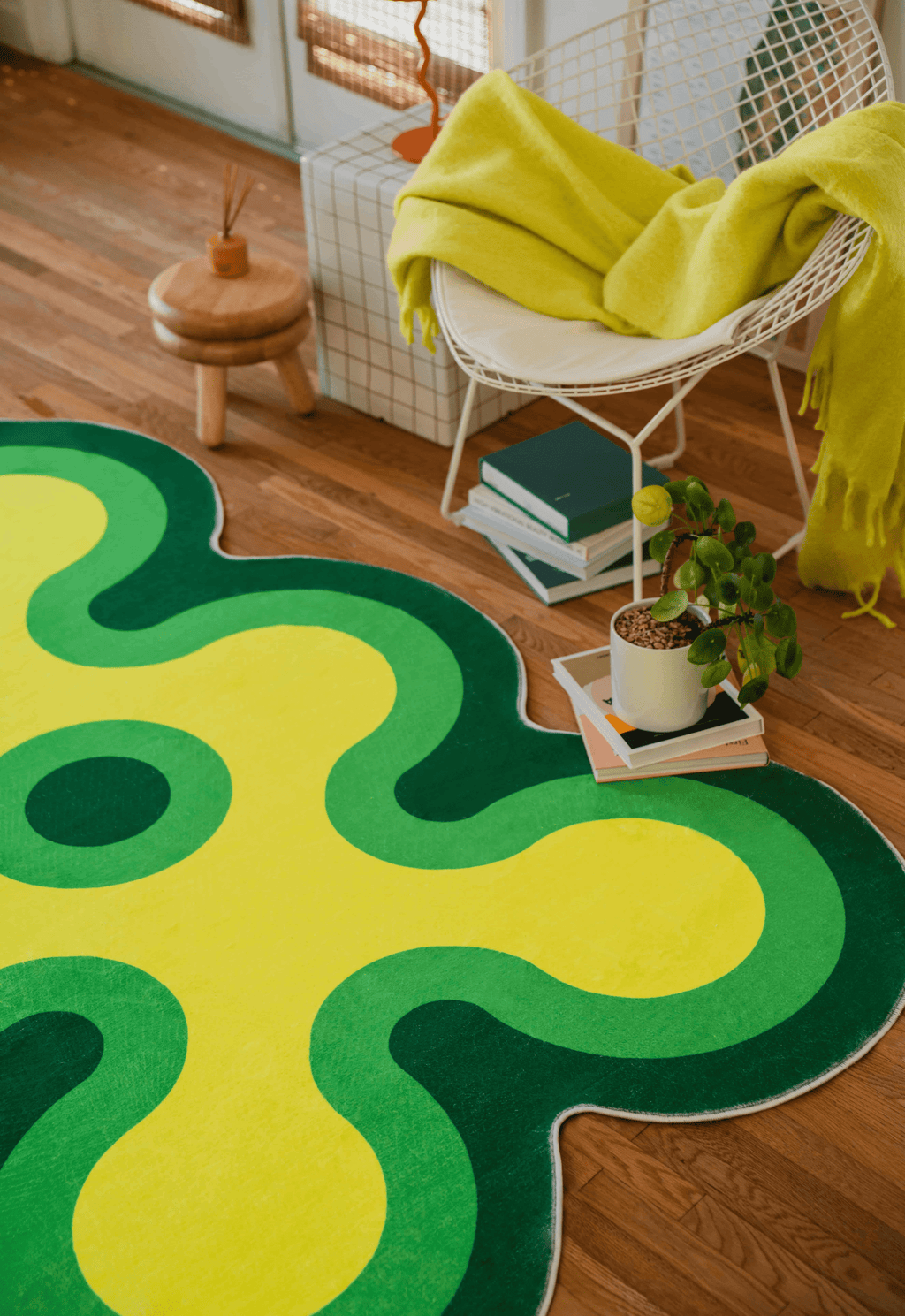 Close-up of the green and yellow coral rug beside a wire chair with a lime throw and stacked books.
