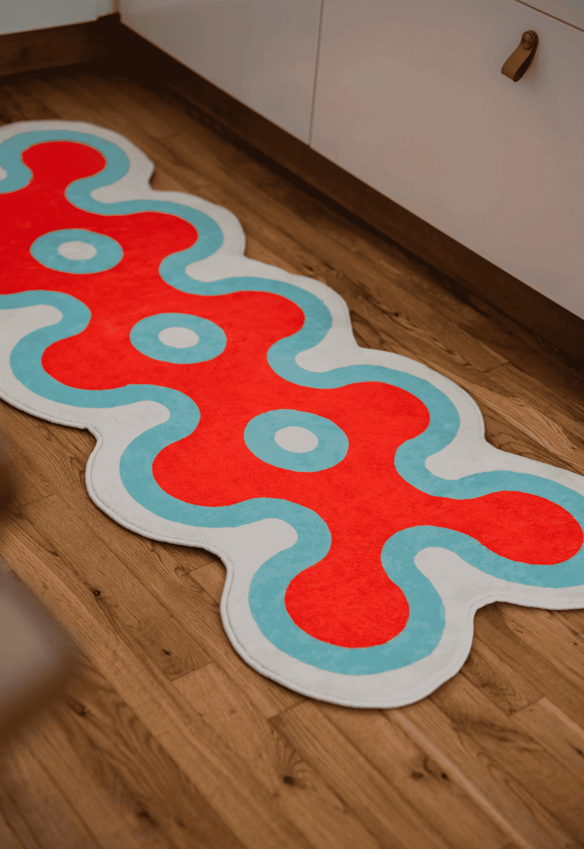 Irregular coral design runner in red, white, and blue on wood floor beside white kitchen cabinets.