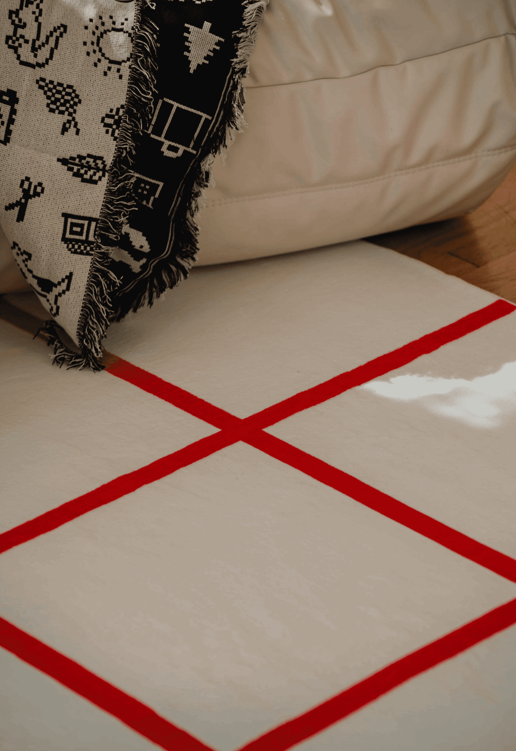Red grid detail of the rug next to a cream sofa and monochrome woven throw, illuminated by soft natural light.