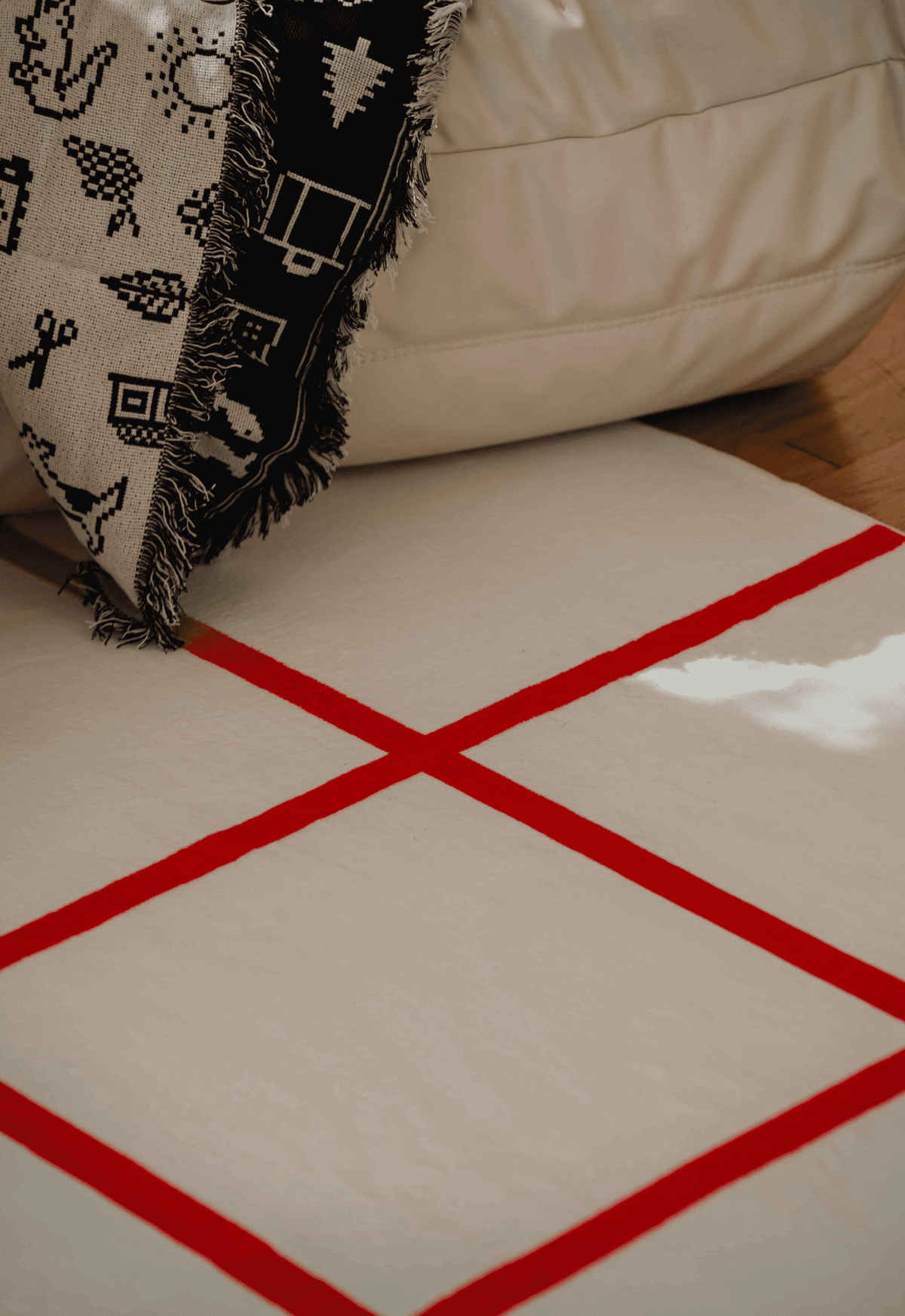Red grid detail of the rug next to a cream sofa and monochrome woven throw, illuminated by soft natural light.
