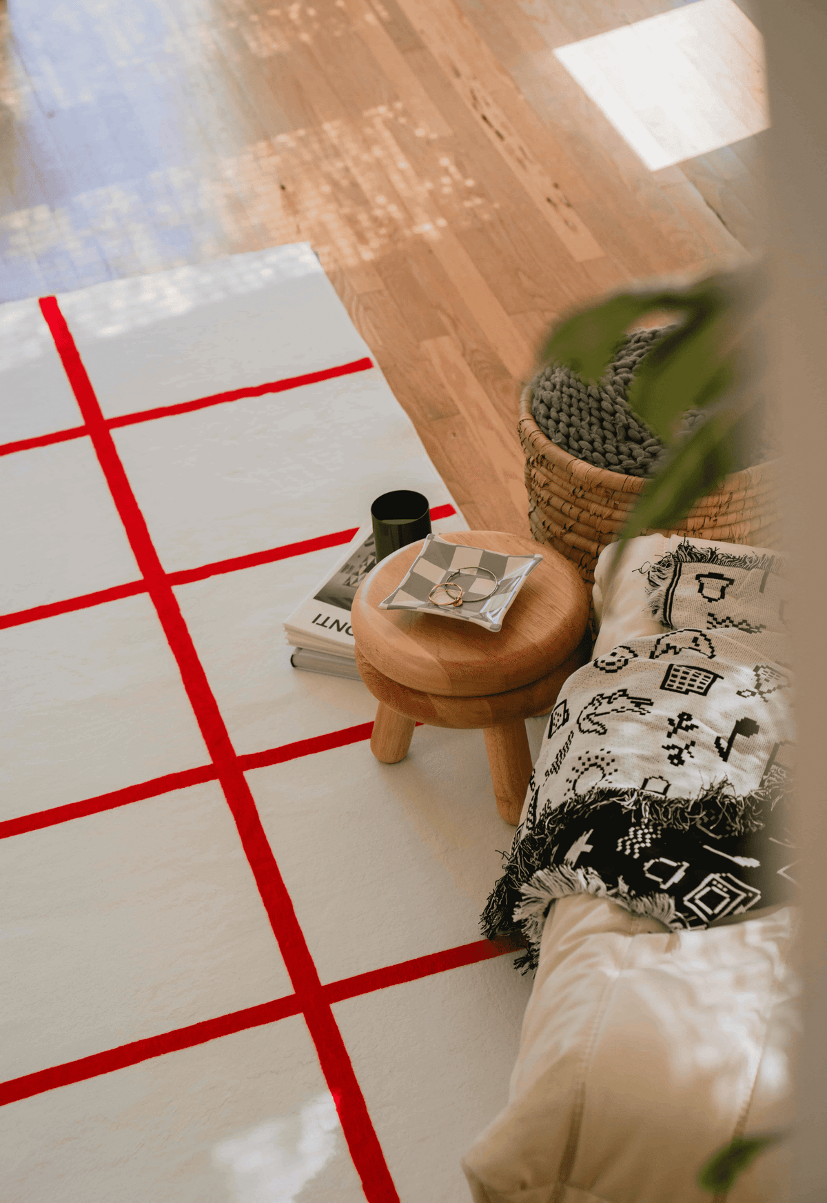 Red and white grid rug under wooden stool with checker tray, black mug, and graphic throw on cream lounger by window