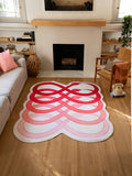 Red abstract loop snake area rug centered between the sofa and fireplace on a light wood floor in a living room