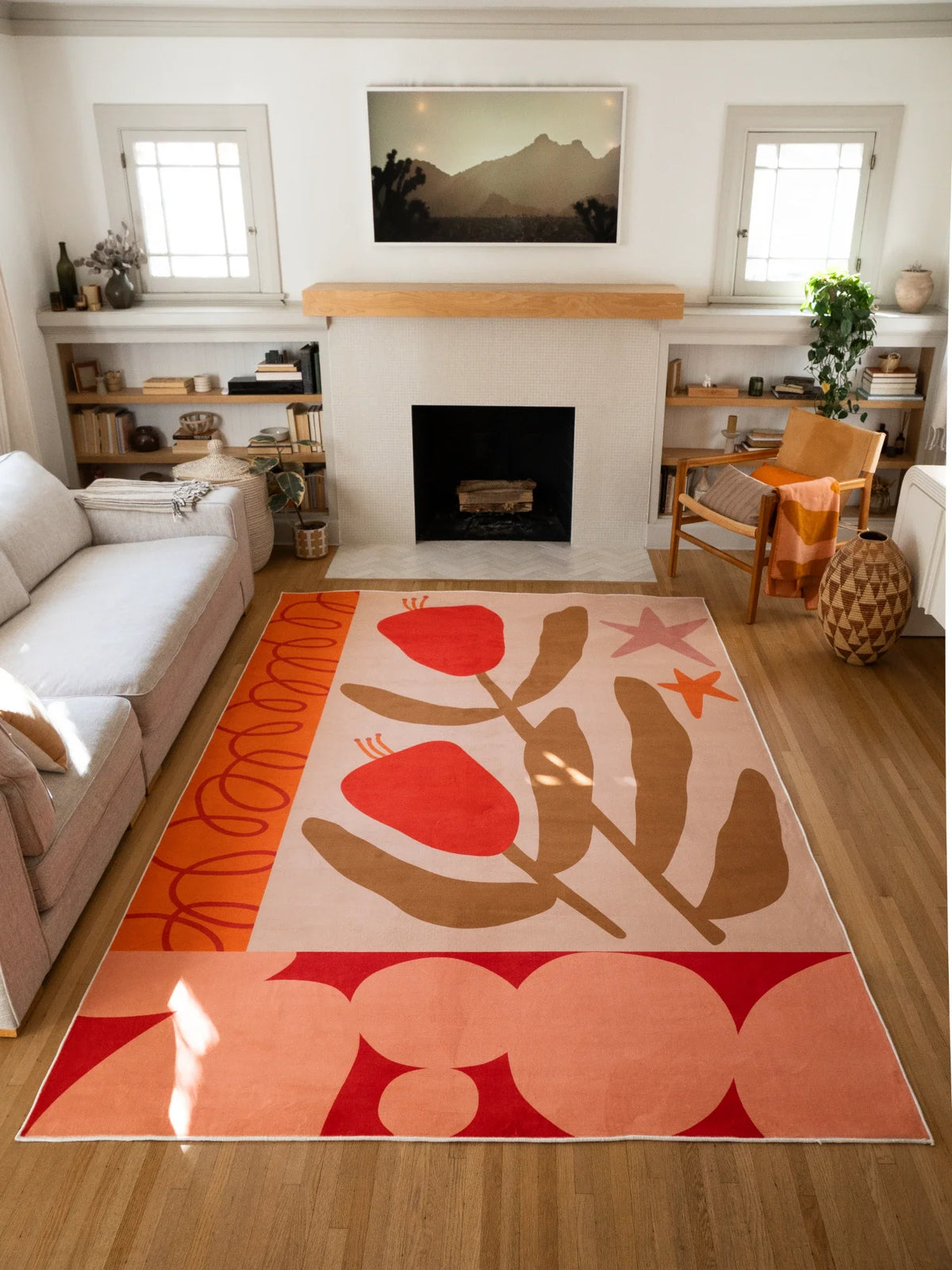 Red Retro Floral Abstract Rug by Sophie Deller in a sunlit living room with a fireplace, sofa, shelving, and wood chair