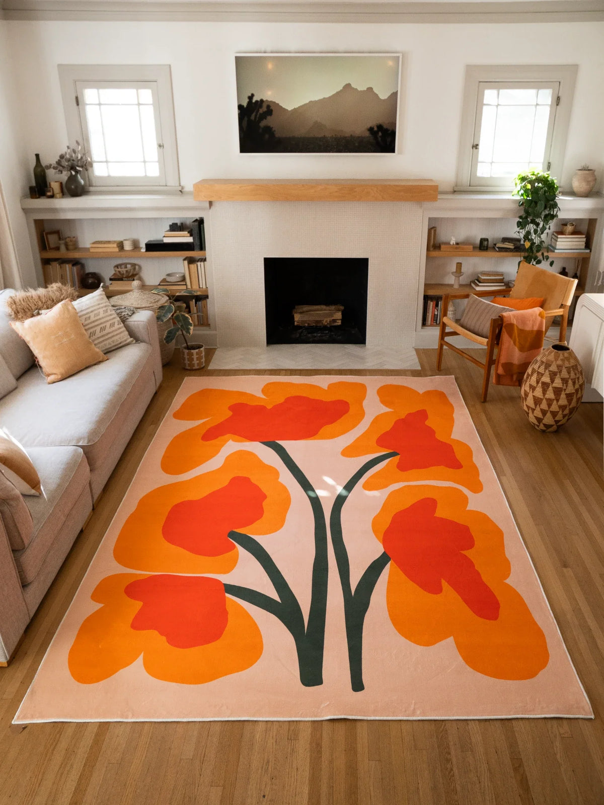 Wide room view of the floral sprig rug placed between a sofa and fireplace, with bold orange blooms and dark stems