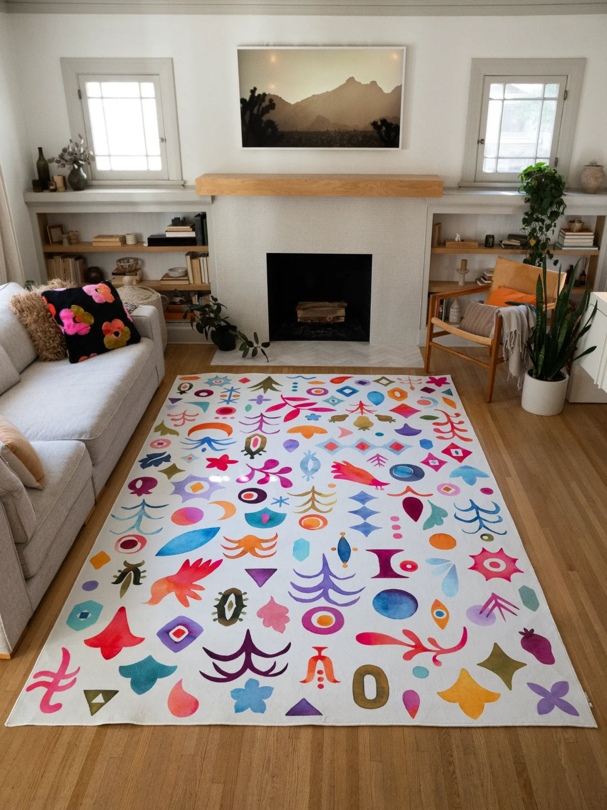 Colorful graphic pattern area rug centered between the sofa and fireplace on a light wood floor, filled with bright nature inspired symbols