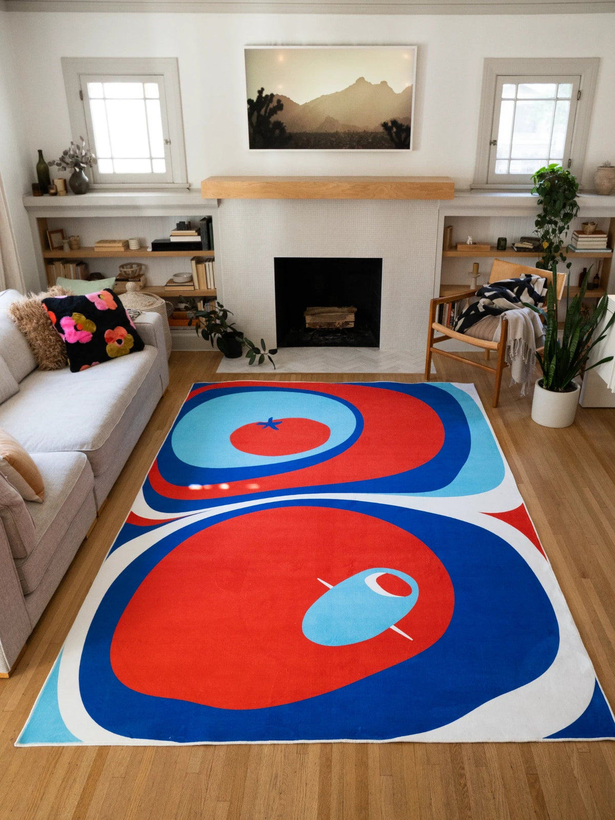 Tomato Twist Abstract Area Rug in blue and red in a bright living room with a fireplace and gray sofa