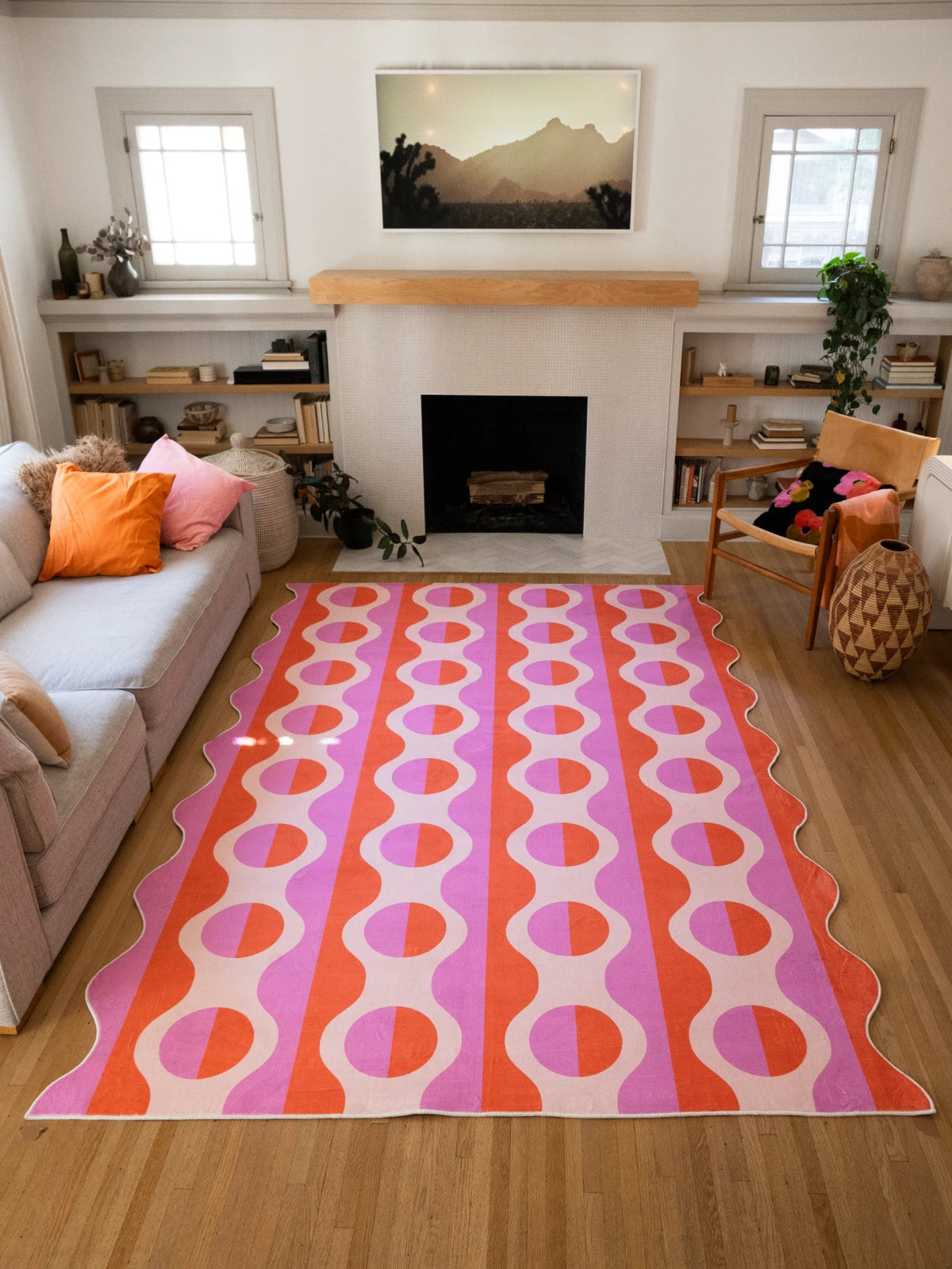 Pink and orange geometric striped area rug stretching between the sofa and fireplace on a light wood floor