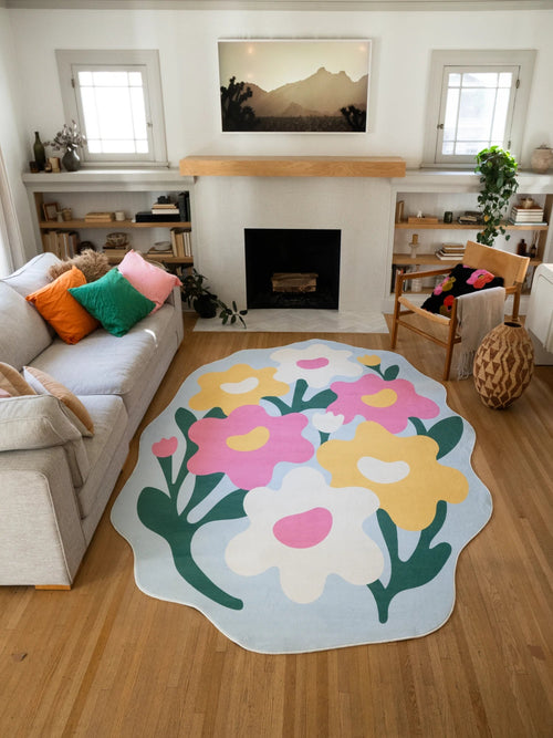 Floral area rug in front of the fireplace, showing hand cut style flower shapes and dark green stems on a pale blue ground