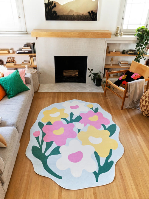 Colorful irregular flower rug centered between the sofa and fireplace on a light wood floor, with oversized pink, yellow, and white blooms