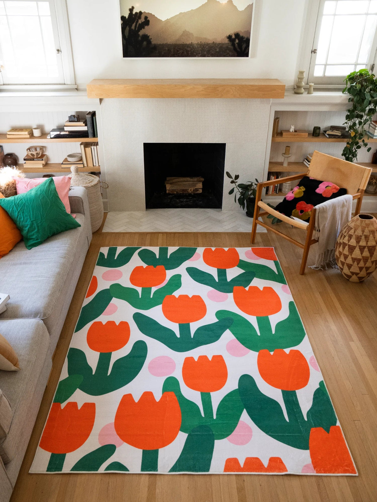 Orange modern floral area rug centered between the sofa and fireplace on a light wood floor, with bold tulip shapes and green leaves