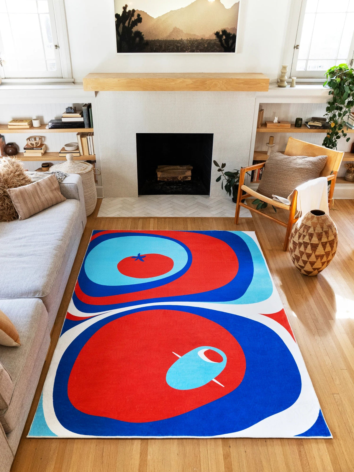 Blue and red Tomato Twist rug in a sunny living room between a sofa and fireplace on a light wood floor