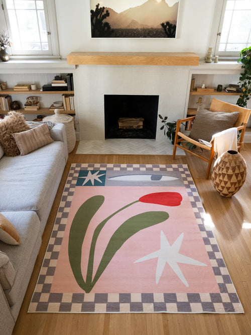 Blush Pink Vintage Checkered Floral Area Rug by Sophie Deller in a sunlit living room with a fireplace, sofa, and wood chair