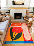 Multicolor Modern Abstract Floral Rug by Sophie Deller centered between the sofa and fireplace, with a red bloom, dark green leaf, and blue border