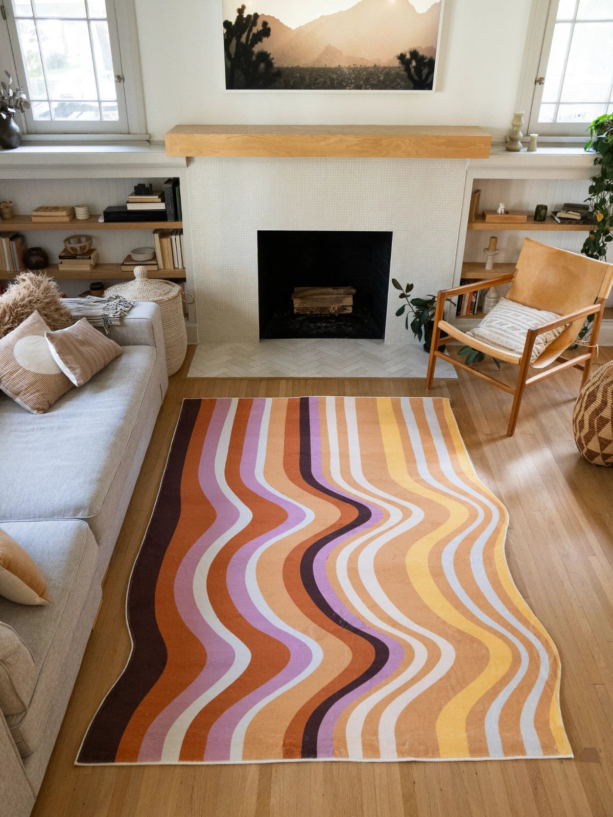 Flowing striped rug framed between a sofa and fireplace, with layered brown, peach, cream, and lilac bands