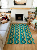 Green and mustard geometric striped area rug centered between the sofa and fireplace on a light wood floor