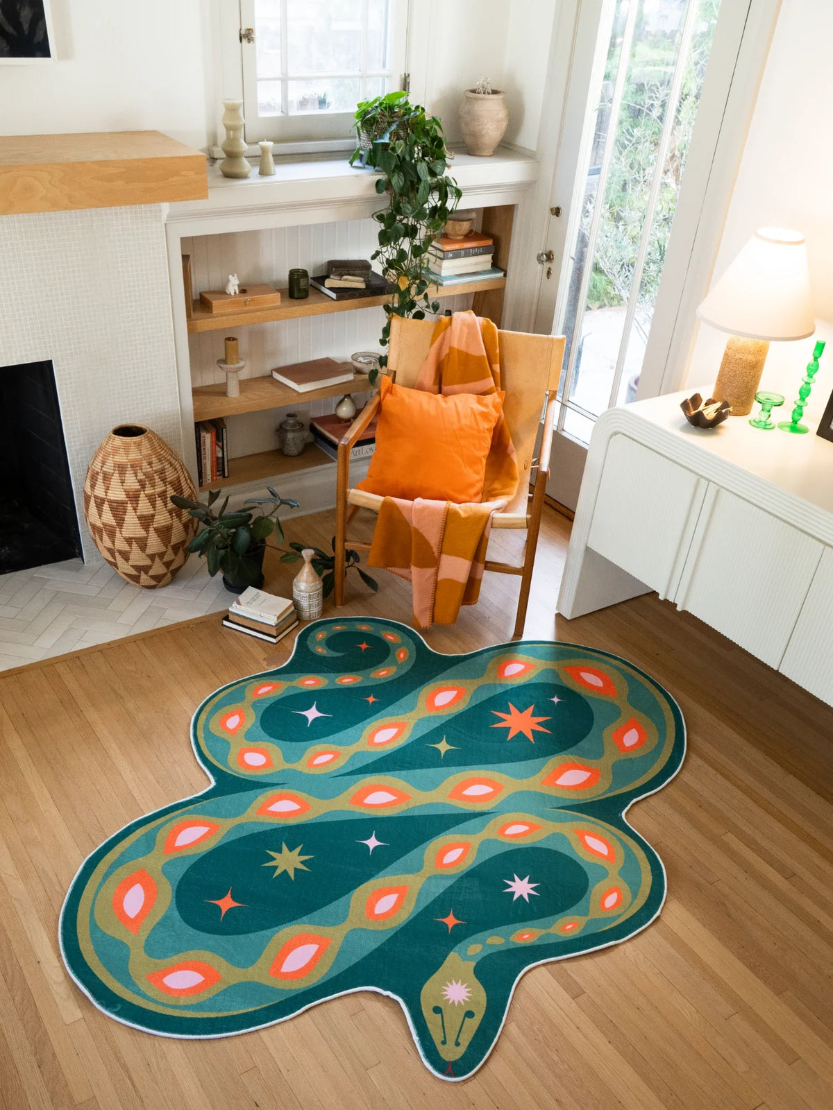 Green abstract snake rug near a white media console and orange chair in a creative living corner