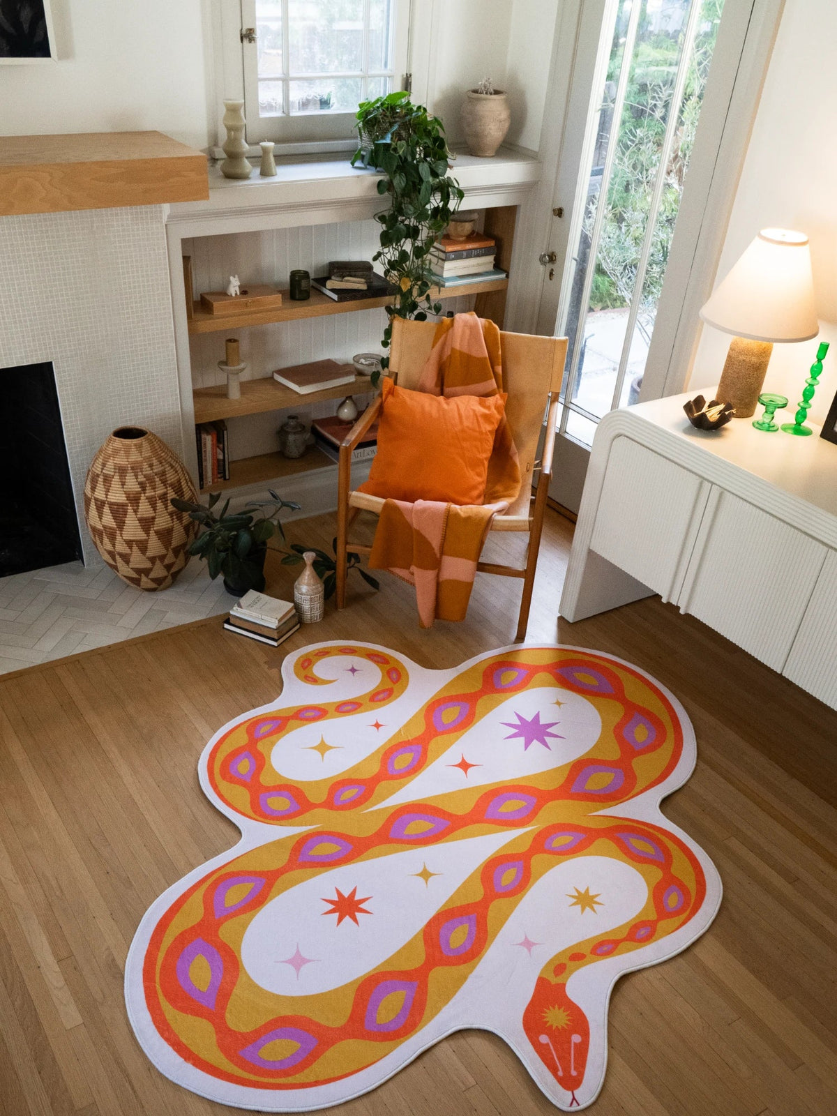 Warm orange snake shaped rug near a white media console and orange chair, with looping body lines and oval spots