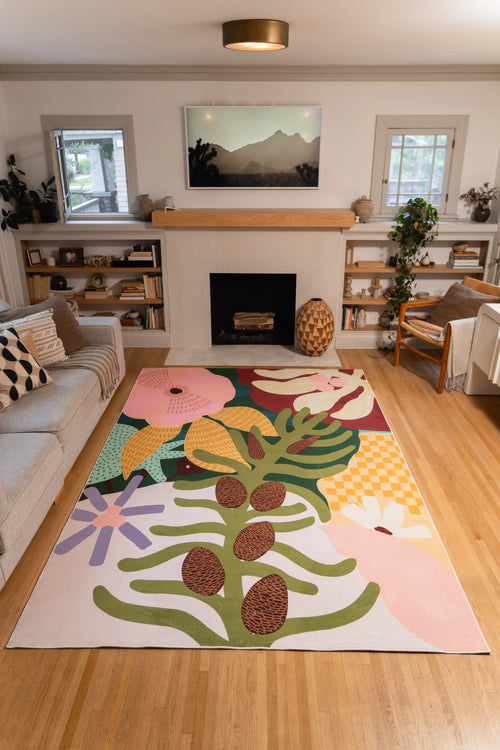 7' × 10' Colorful Tropical Flower Rug by Qiao Yu with oversized pink, cream, and lavender flowers and green leaves in front of a fireplace.