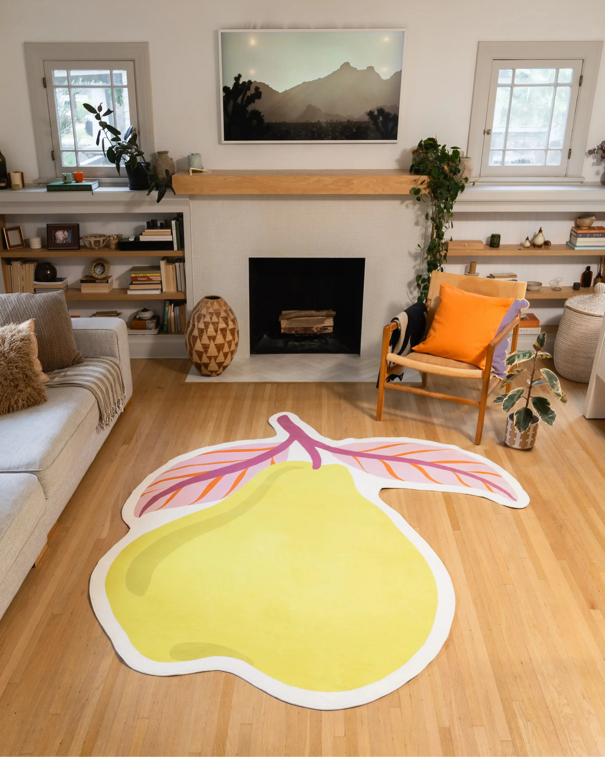 7' × 8' Yellow Irregular Pear Rug by Maayan Alper-Swan with a yellow pear, blush leaves, mauve stem, orange veins, and white border in front of a fireplace.