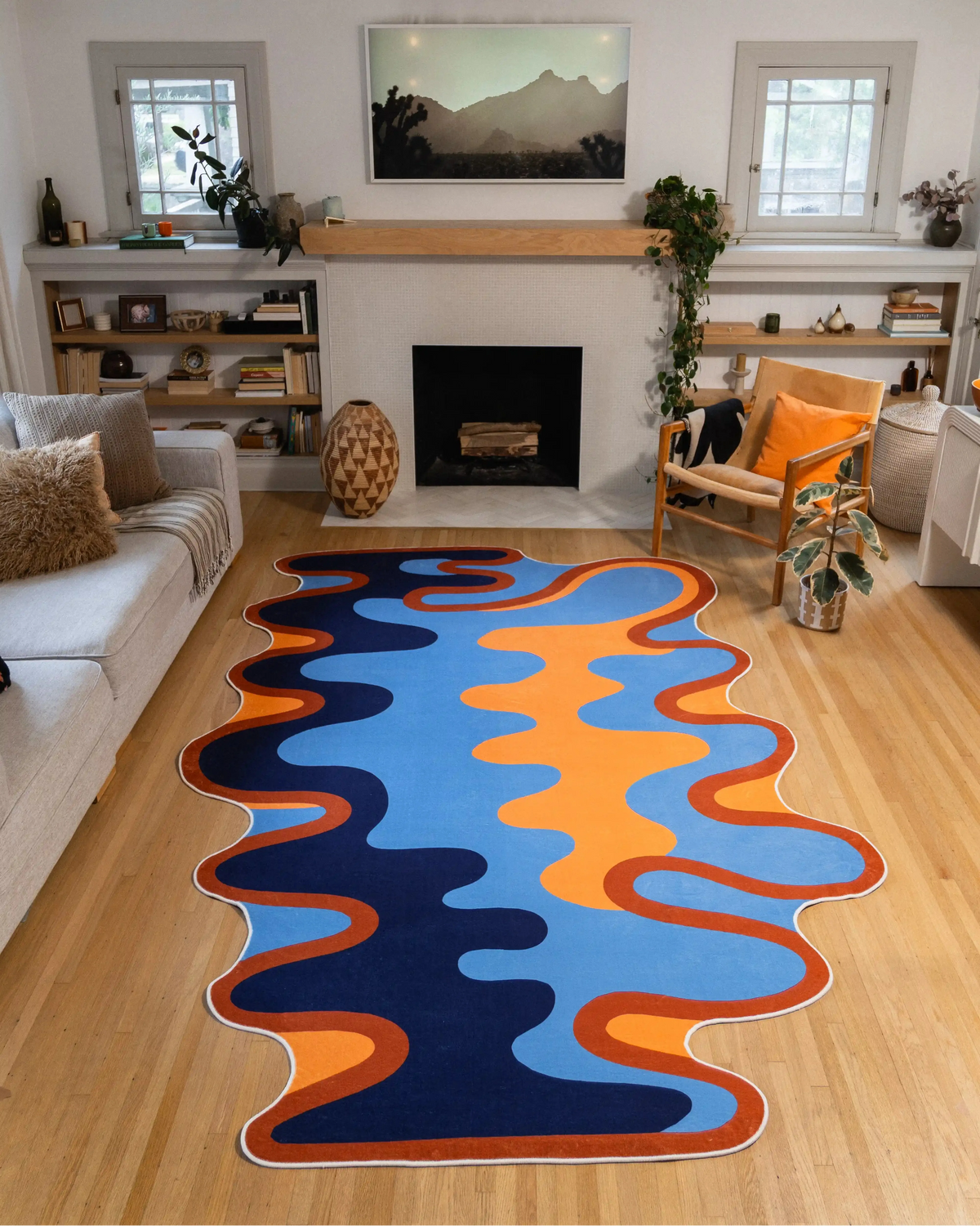 The 7' × 10' Irregular Blue Abstract Wave Rug by Ariana Berman fills the space between a gray sofa and wooden chair, with its wavy outline fully visible on the wood floor.
