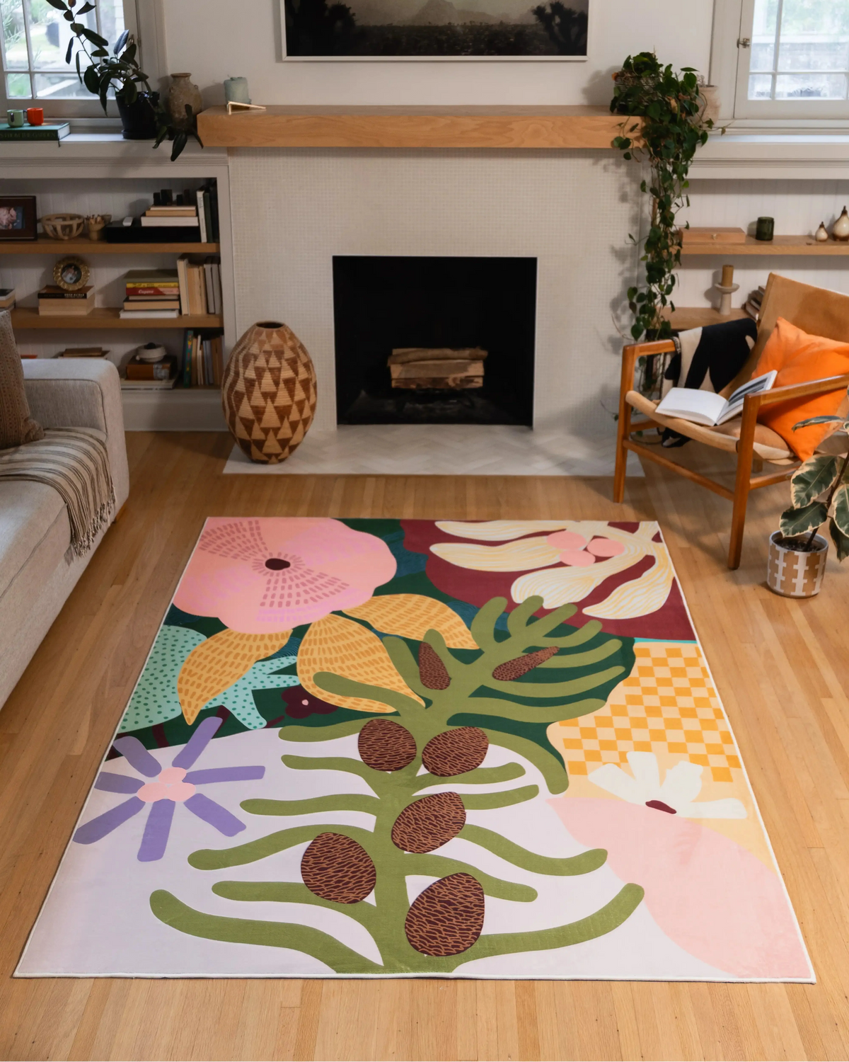 5' × 7' floral rug with pink and cream blooms, green leaves, brown seed pods, and yellow checks between a gray sofa and wooden chair.
