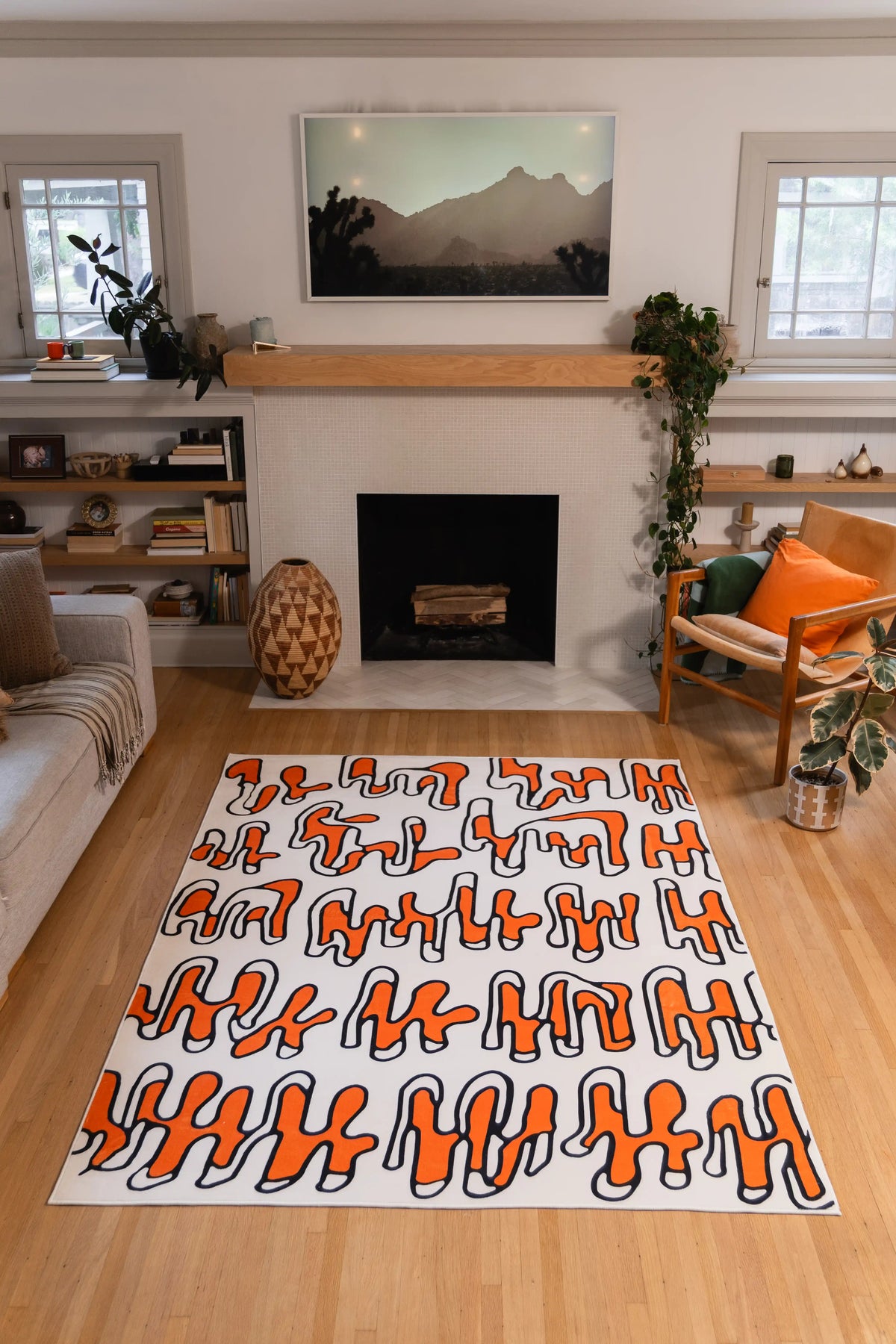 A rectangular area rug with an abstract wavy pattern in orange, black, and white, styled on a light wood floor in a modern living room setting.