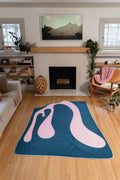 The 5' × 7' blue and pink version sits in front of the fireplace with the surrounding wood floor visible.