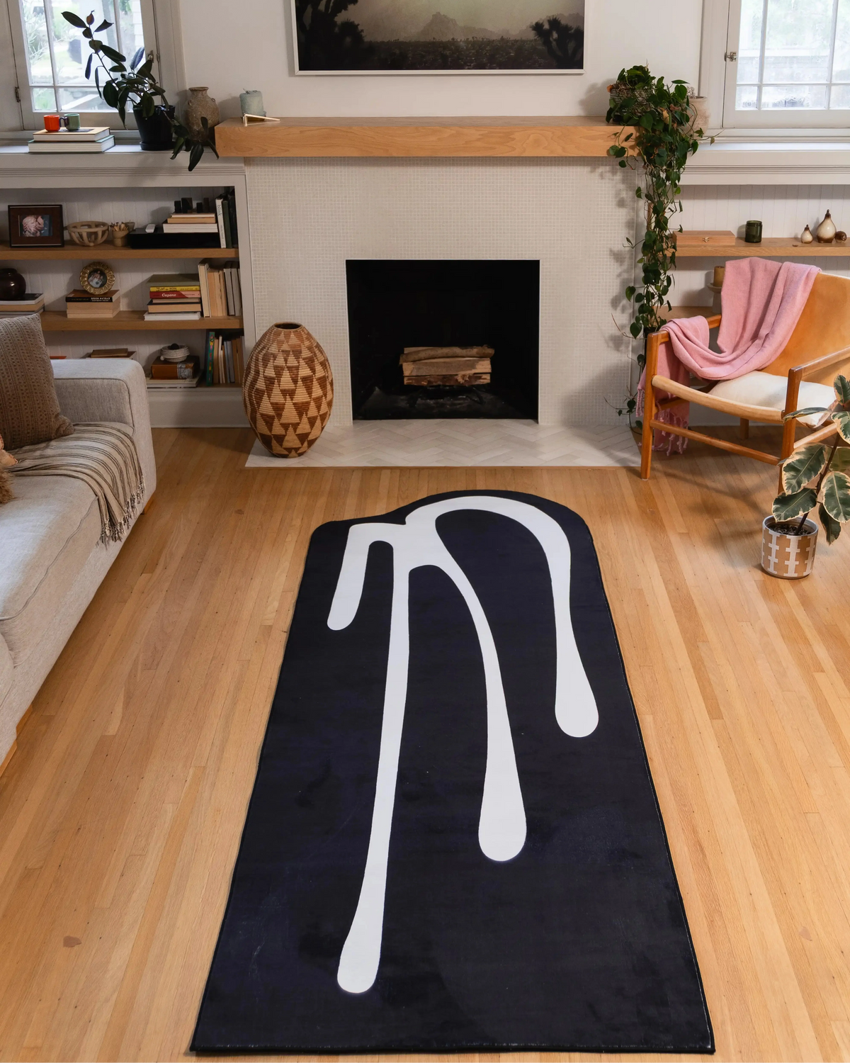 3' × 9' black rug with flowing white drip lines centered on light wood flooring in front of a fireplace.