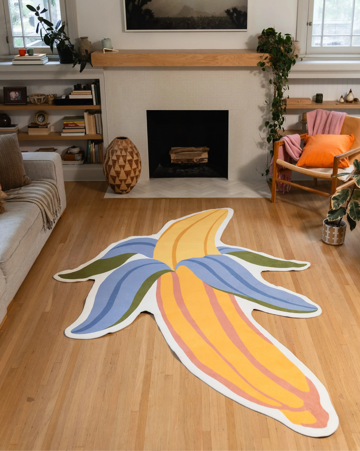 7' × 8' Yellow Irregular Banana Rug by Maayan Alper-Swan with yellow fruit, blue and green peel sections, and a white outline in front of a fireplace.