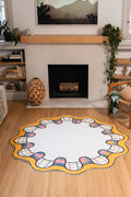 6' × 6' Yellow Scalloped Plaid Border Rug by Ariana Berman with a cream center, golden wavy rim, and multicolor plaid loops in front of a fireplace.
