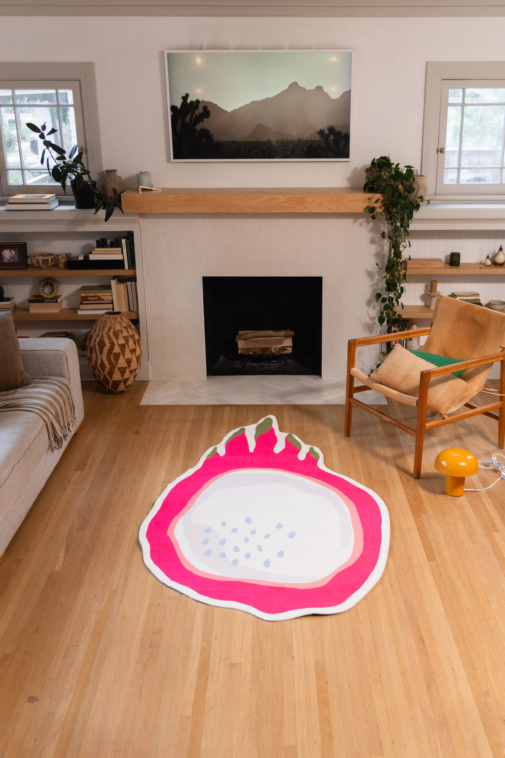 4' × 7' sliced dragon fruit rug with a pink rind and pale seeded center on a wood floor in front of a fireplace.