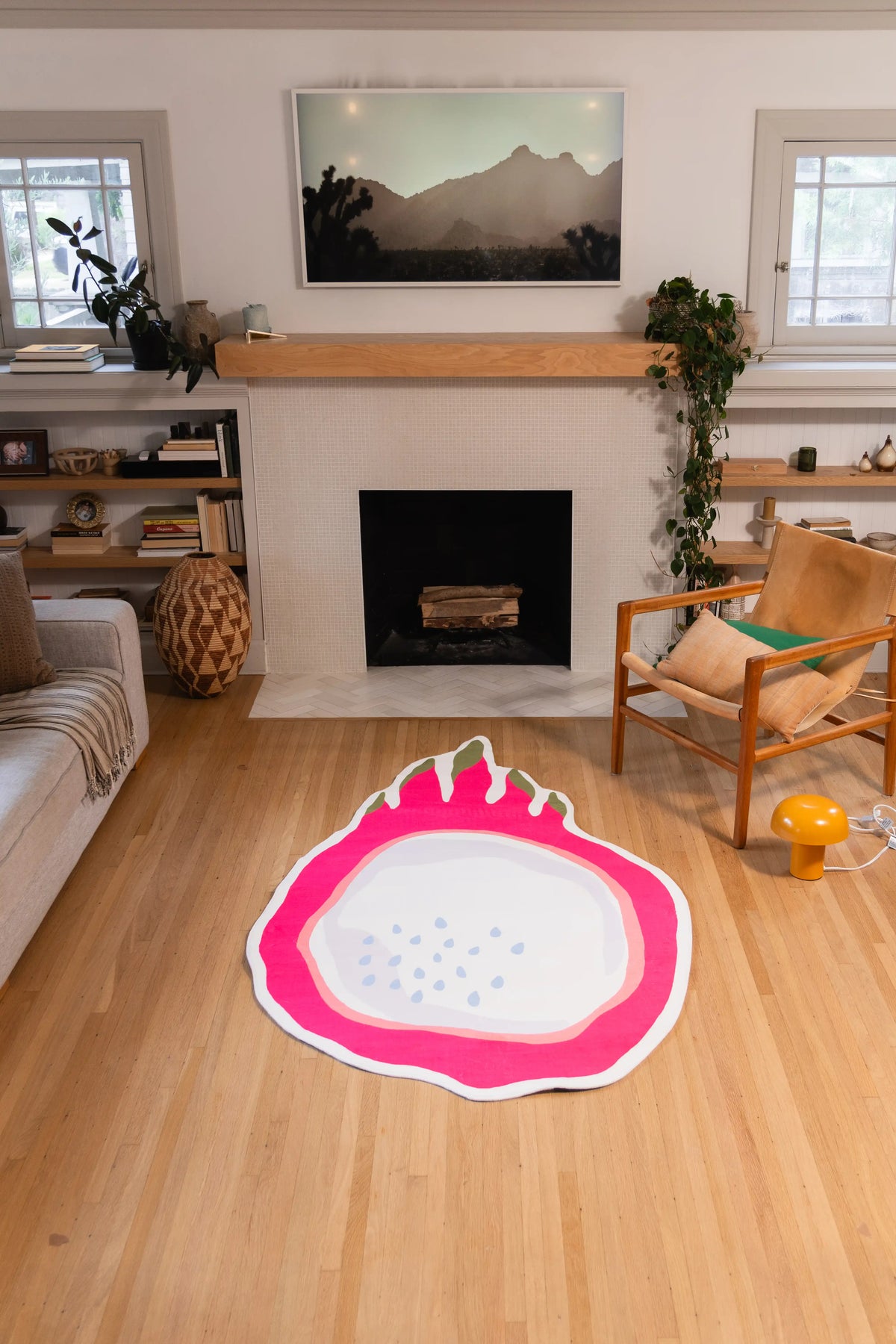 4' × 7' sliced dragon fruit rug with a pink rind and pale seeded center on a wood floor in front of a fireplace.