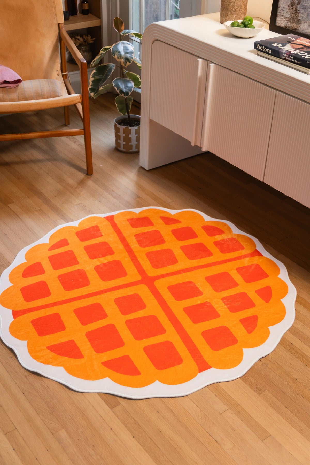 4' × 4' Yellow Irregular Waffle Rug by Becca Franks with orange grid lines and a cream scalloped border beside a white cabinet.