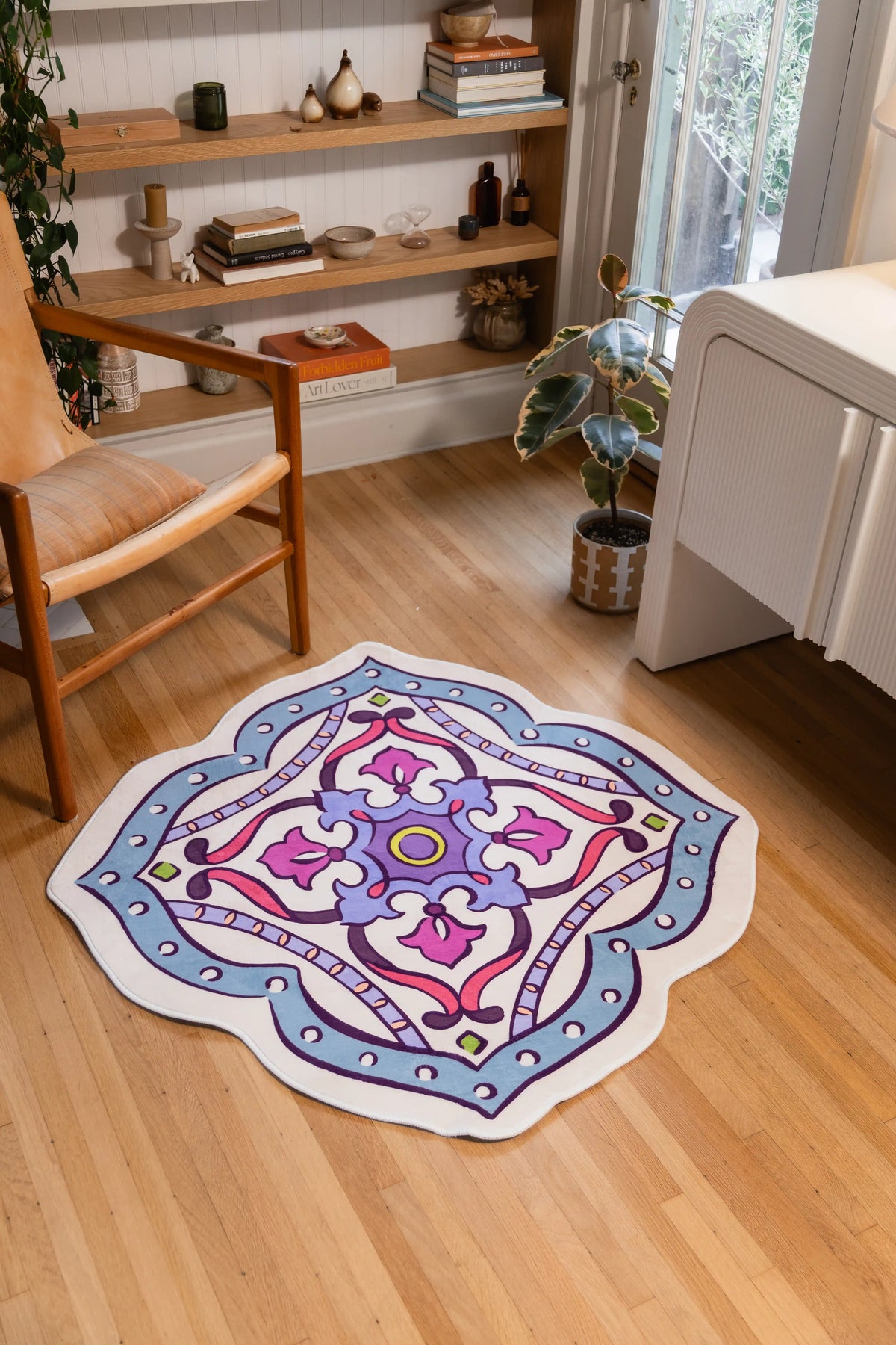 Vintage medallion rug with scalloped edges on wood floor beside a wooden chair and white cabinet.